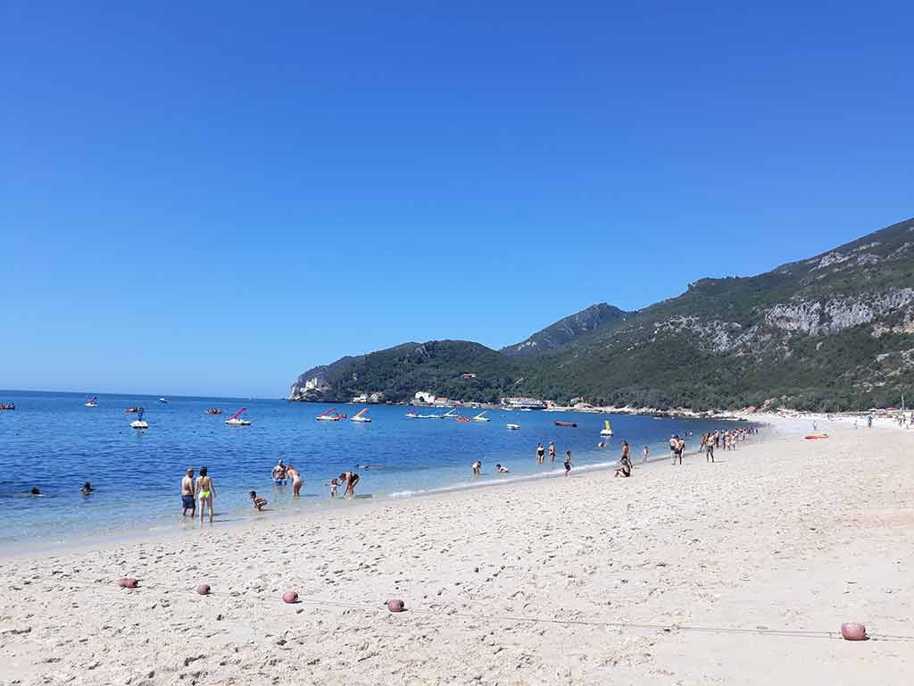 View of the Praia Albarquel in Setubal in summer with people swimming and laying on the sand